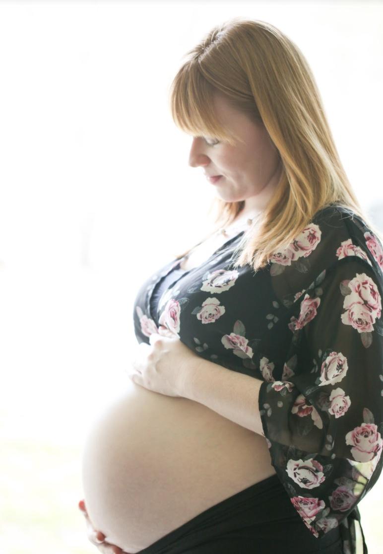 Pregnant woman in a floral top looking down at her bump in soft window light