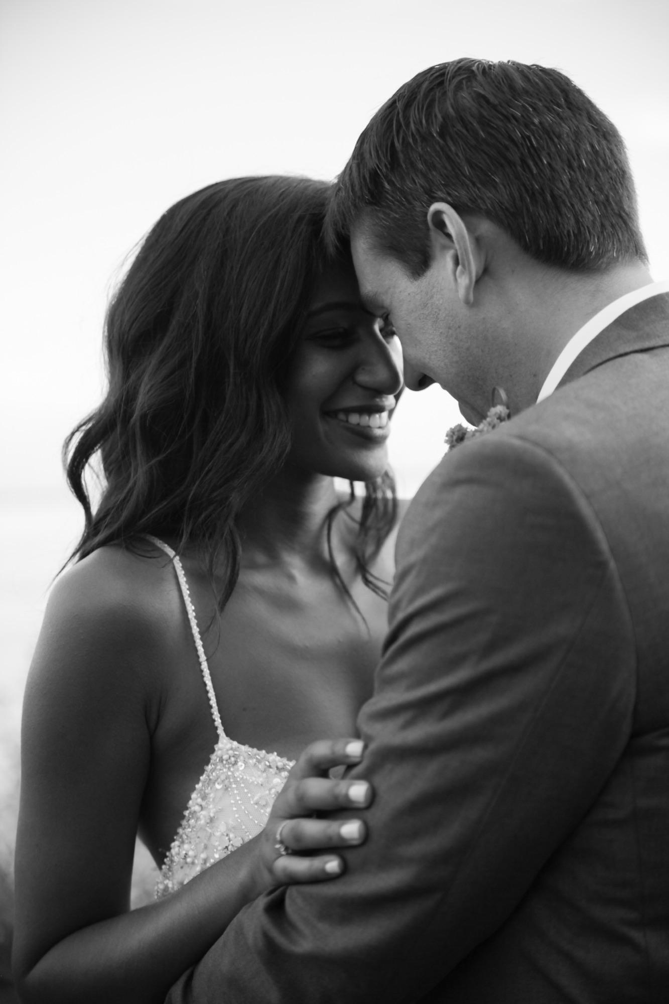 Close black and white portrait of a bride and groom smiling with their foreheads together