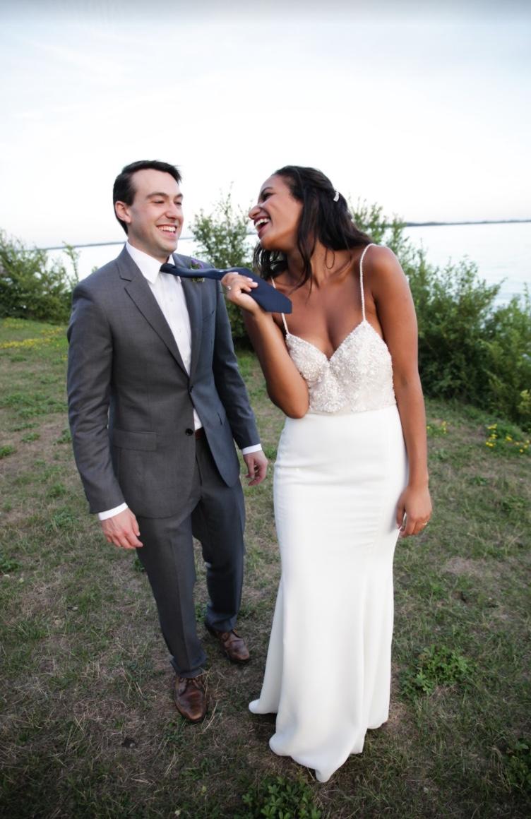 Laughing bride pulling the groom along by his tie on a grassy lakeshore