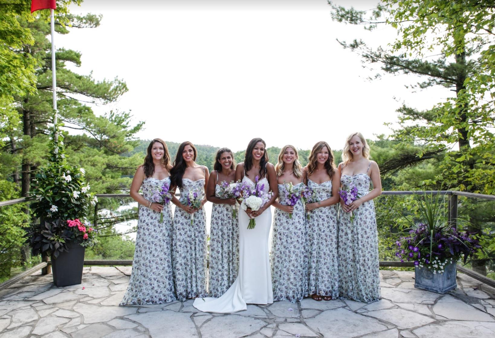 Bride with seven bridesmaids in matching floral dresses on a flagstone terrace above the lake