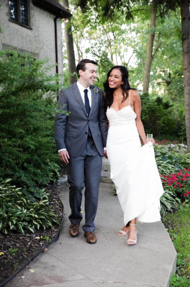 Bride and groom walking hand in hand along a garden path beside a stone house