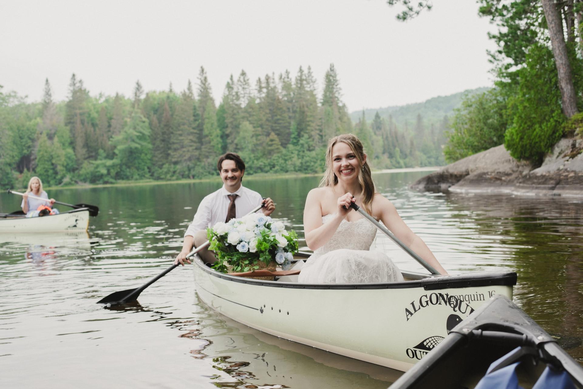 Bride and groom paddling a canoe on a still lake after their ceremony