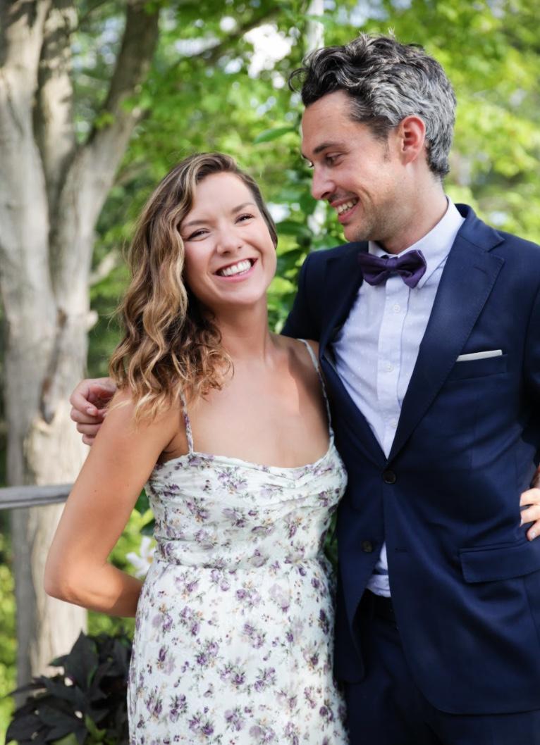 A bridesmaid in a floral dress and a guest in a navy suit and bow tie, smiling in the garden