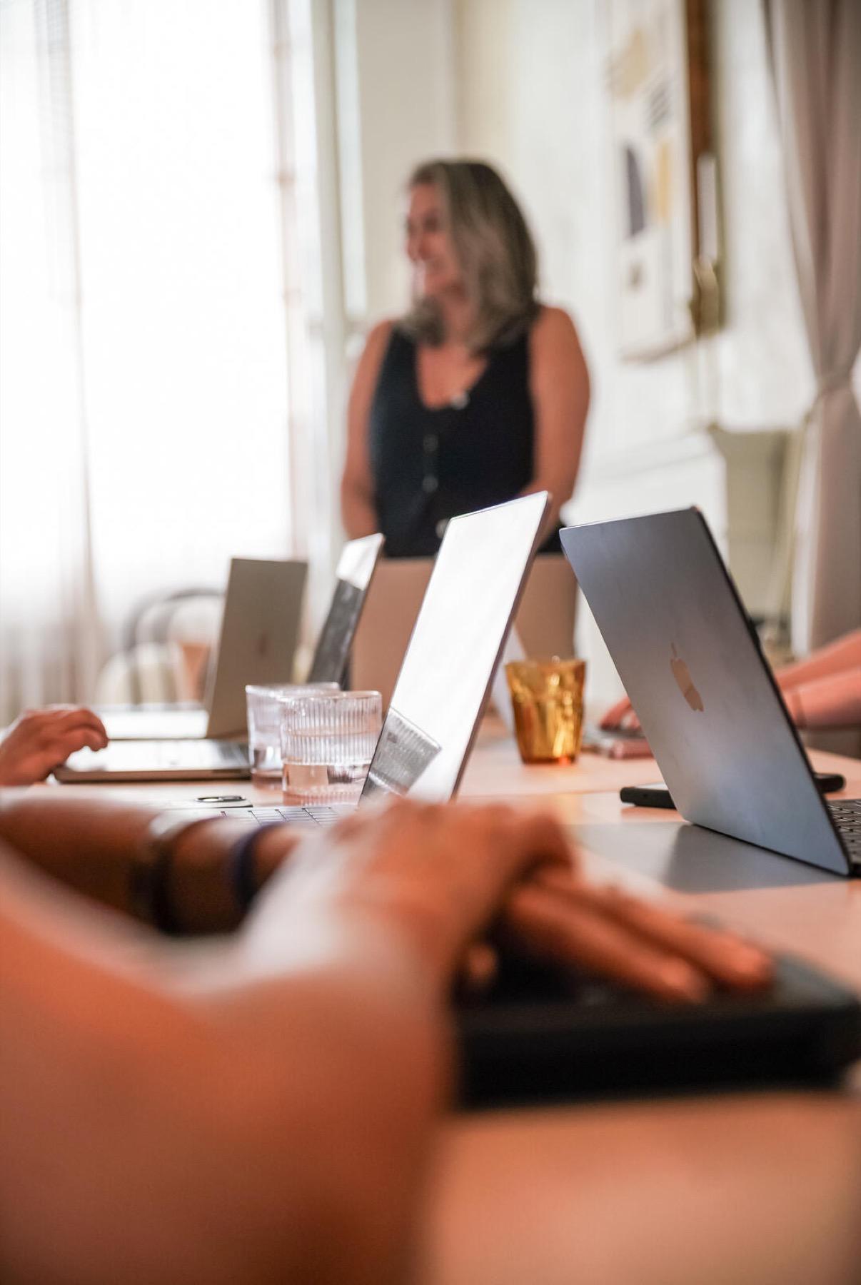Open laptops along a workshop table with a facilitator speaking in the background