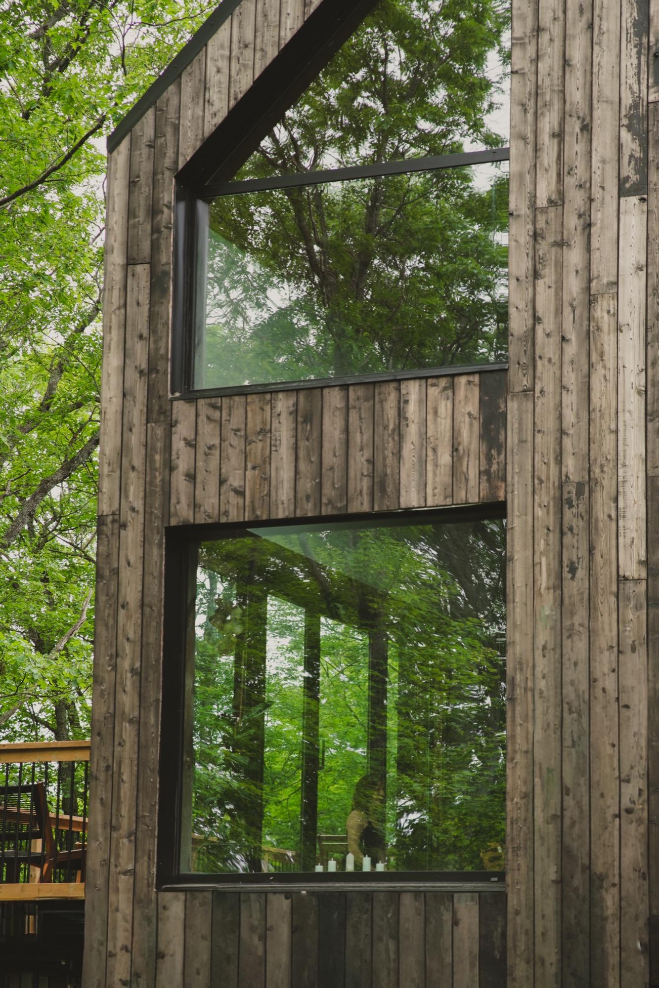 Weathered timber exterior of the retreat building with forest reflected in tall black-framed windows