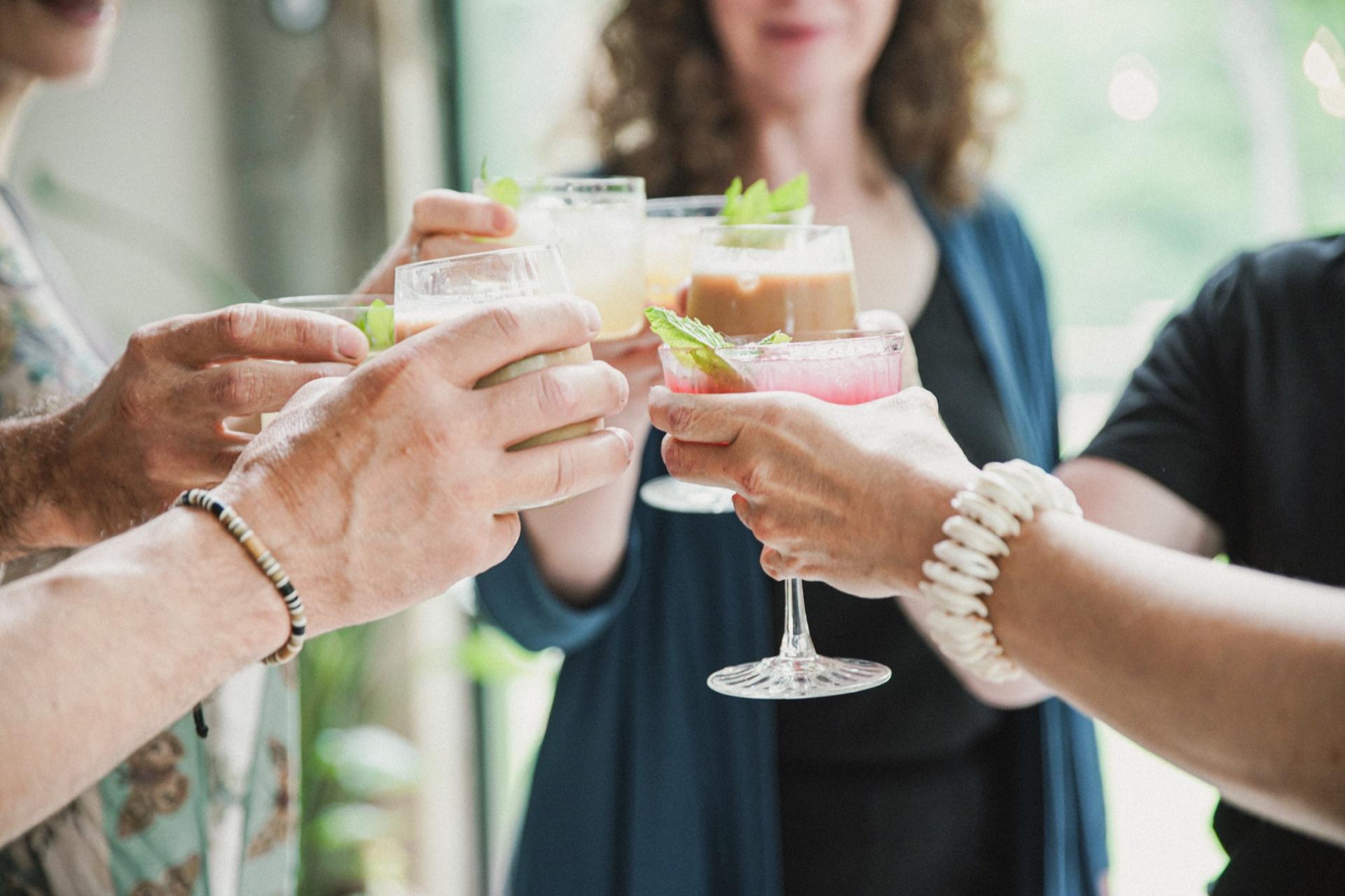 Six hands meeting in the middle of a frame to toast with garnished drinks