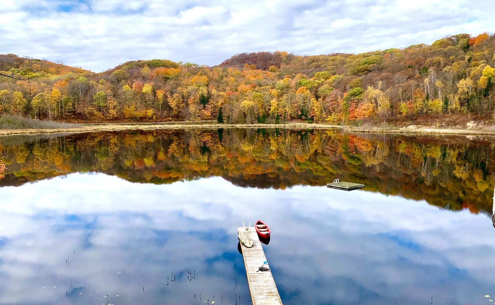 Wooden dock and red canoe on a mirror-still lake with autumn hills reflected in the water
