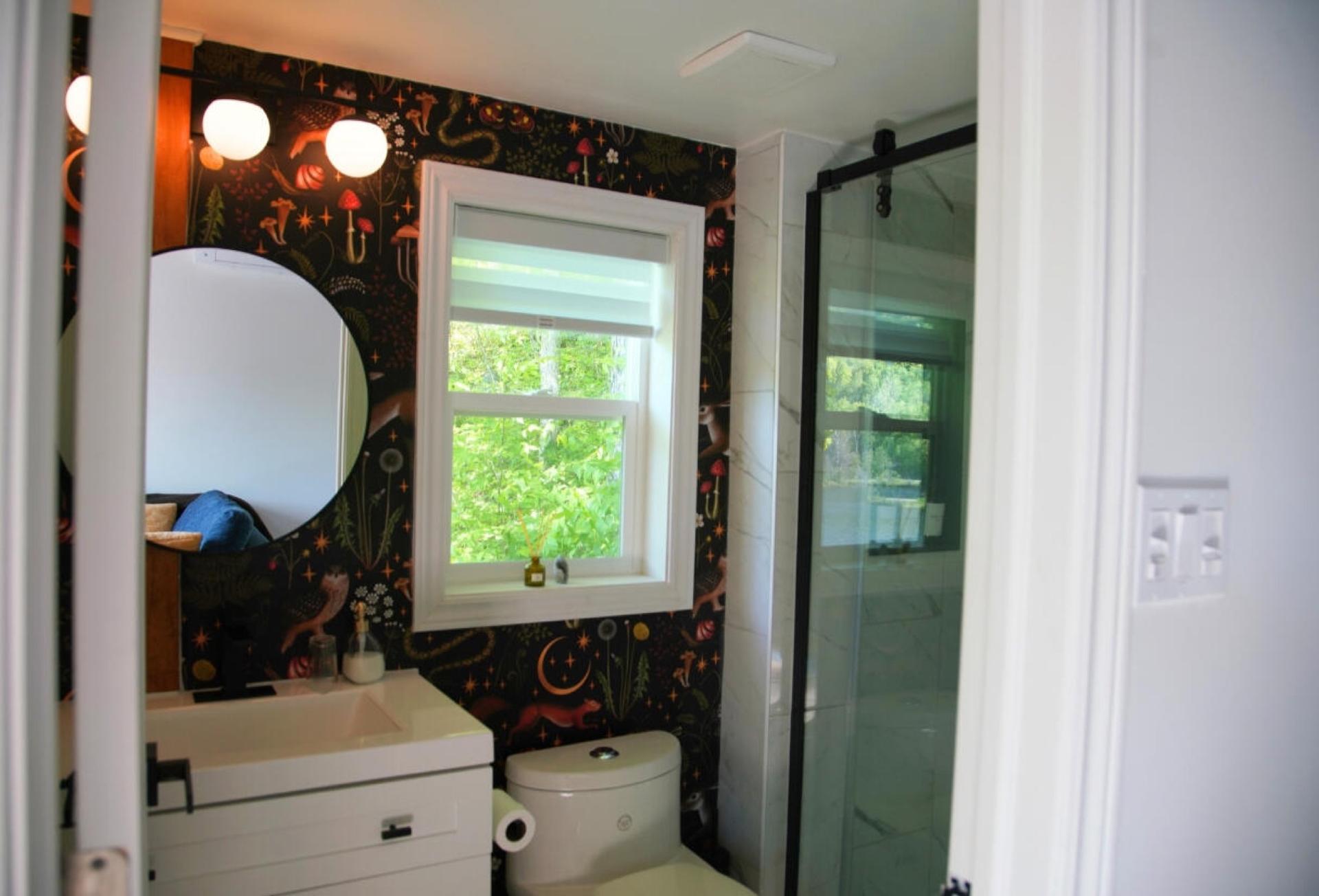Cabin bathroom with dark forest-print wallpaper, a round mirror and a walk-in shower