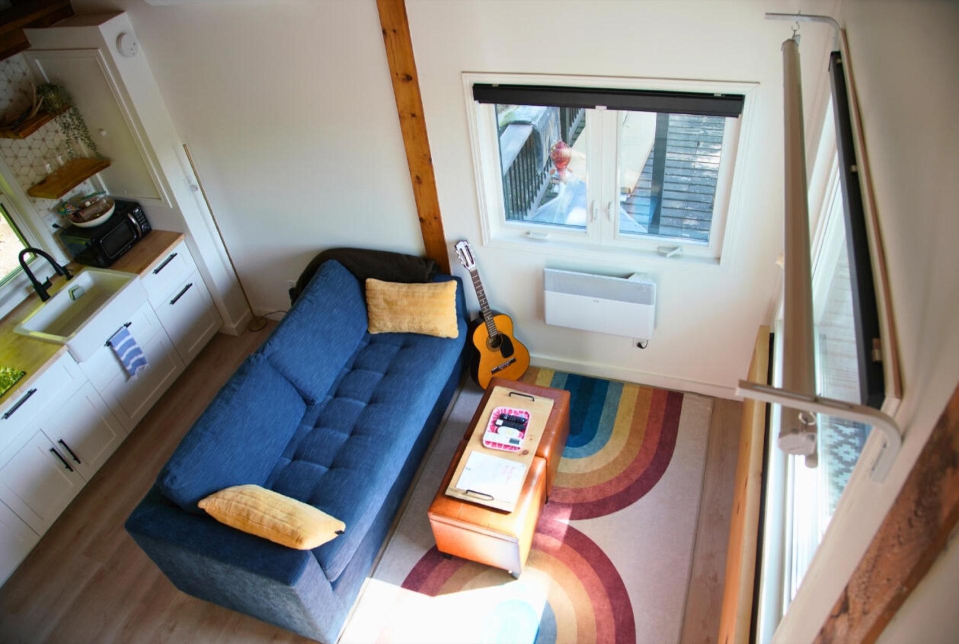 Living area seen from the loft, with a blue sofa, a guitar on the wall and a striped rug