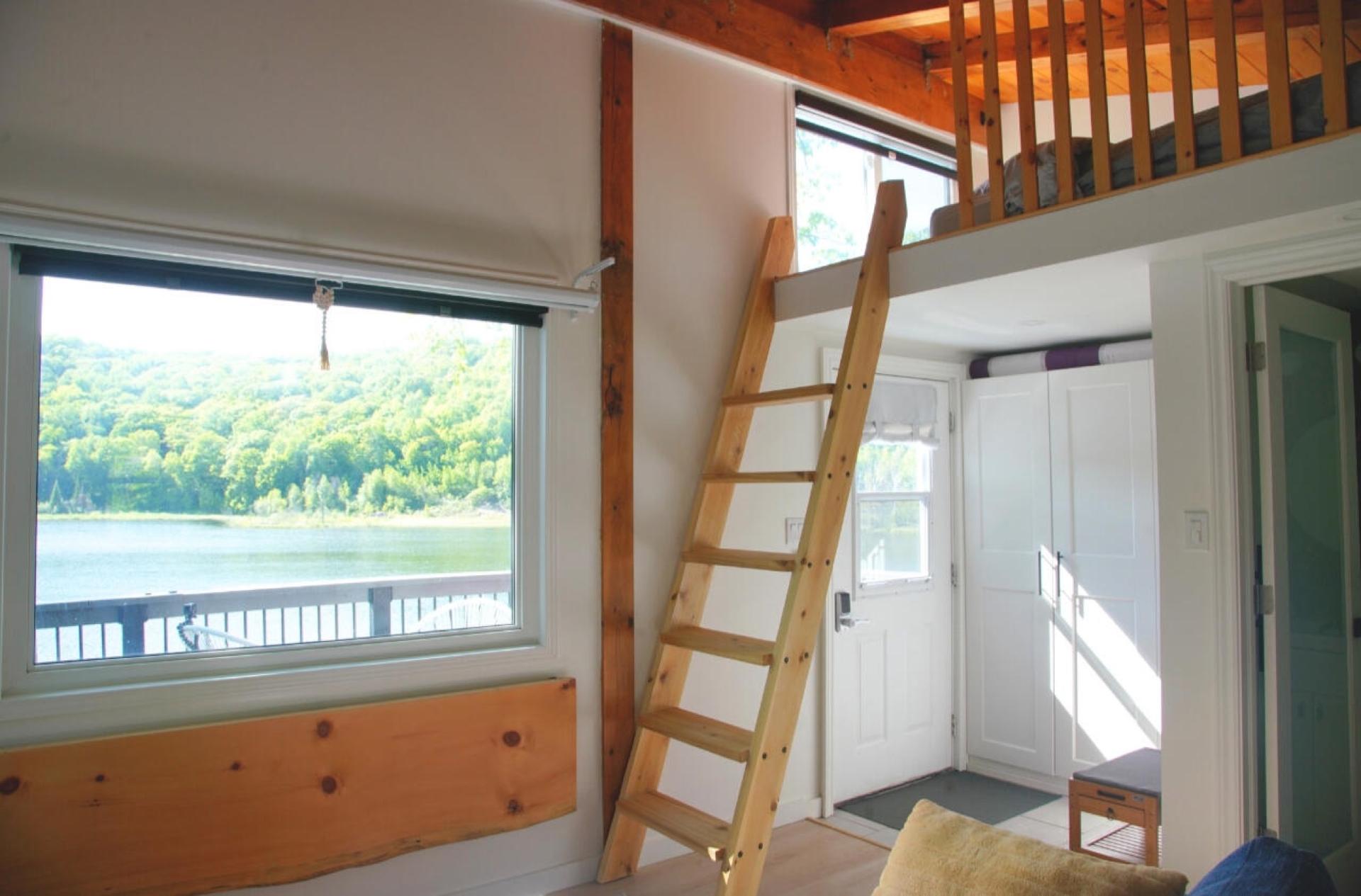 Custom wooden ladder up to the sleeping loft beside a wide window onto the lake