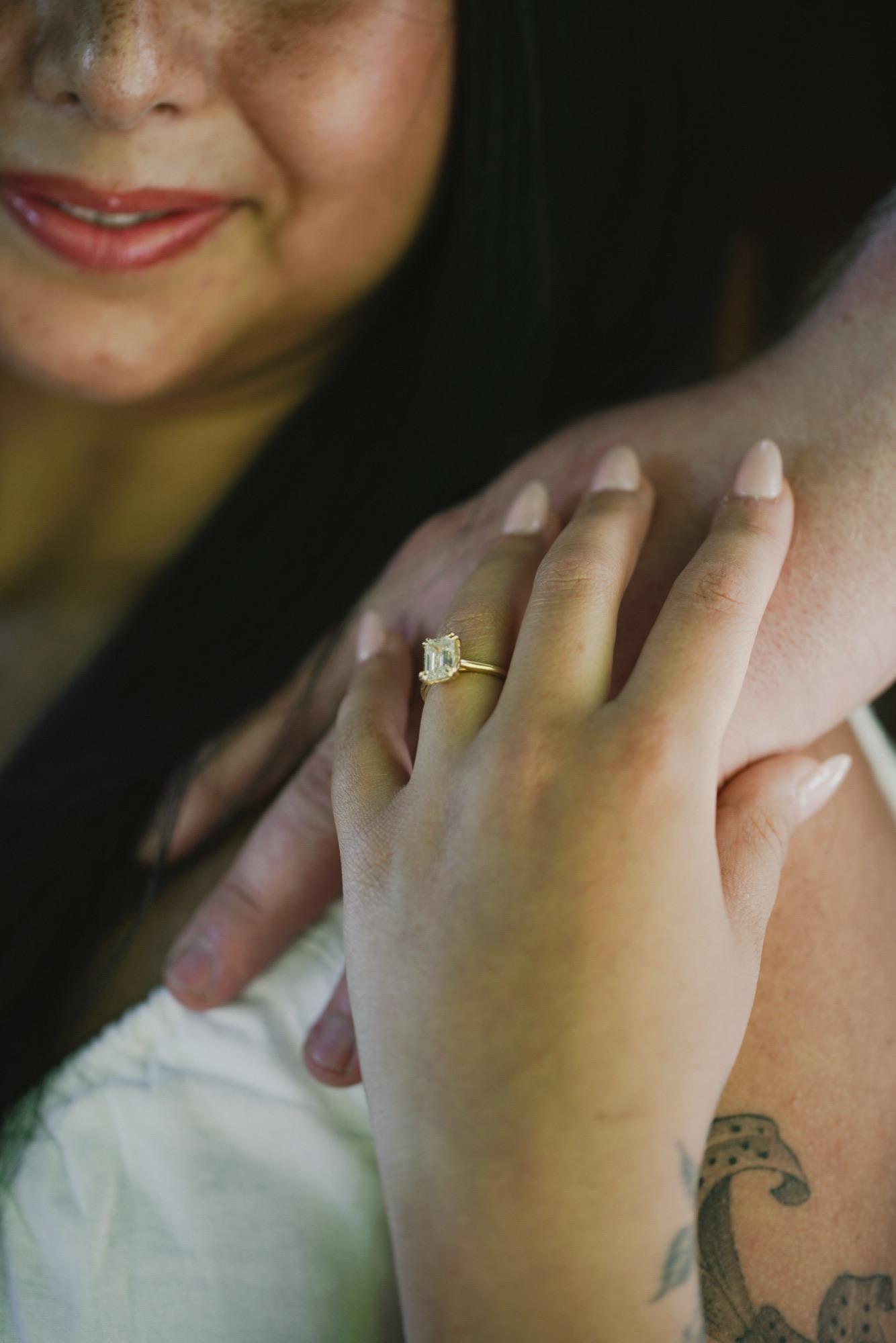 Close detail of an engagement ring on a hand resting on a partner's shoulder