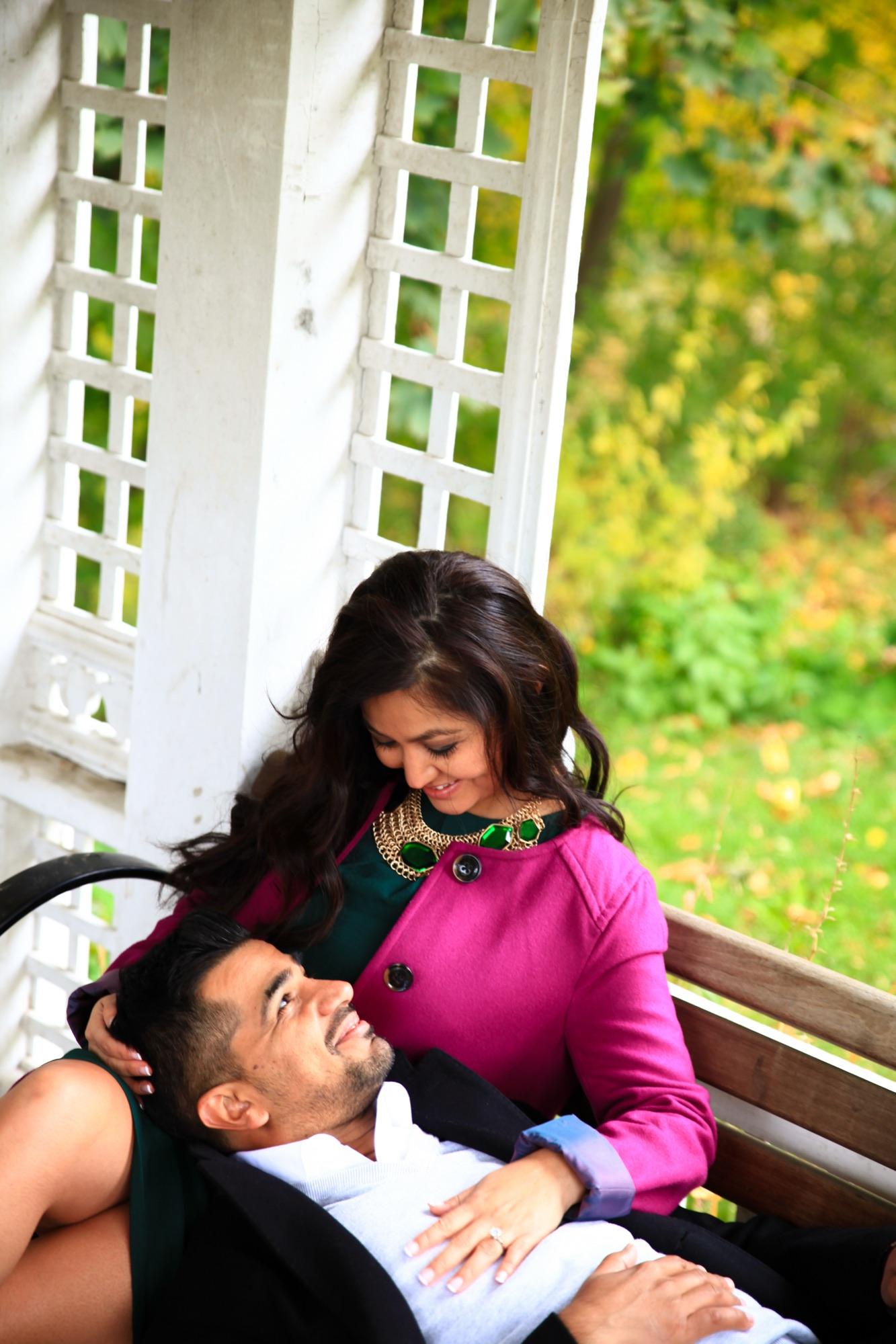 Couple sitting together on a gazebo bench in autumn, one resting across the other's lap