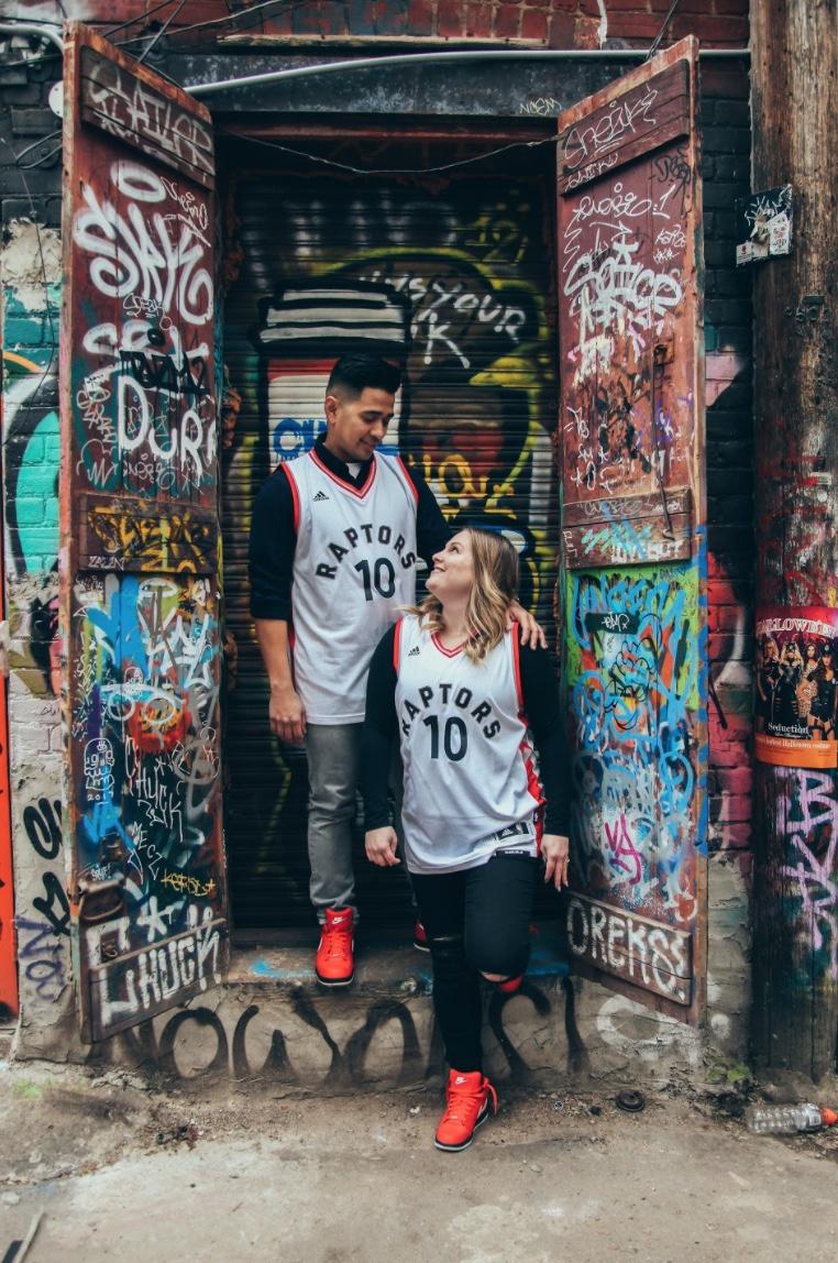 Couple in basketball jerseys standing in a graffiti-covered doorway
