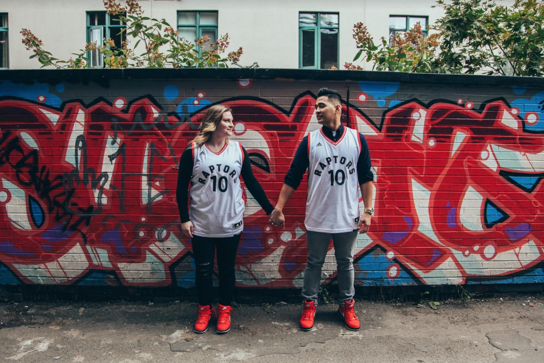 Couple in matching basketball jerseys holding hands in front of a red and blue graffiti wall