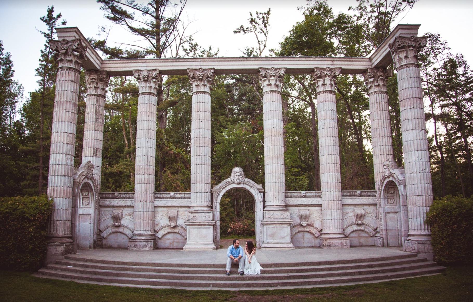 Couple sitting on the steps of a stone colonnade, surrounded by trees