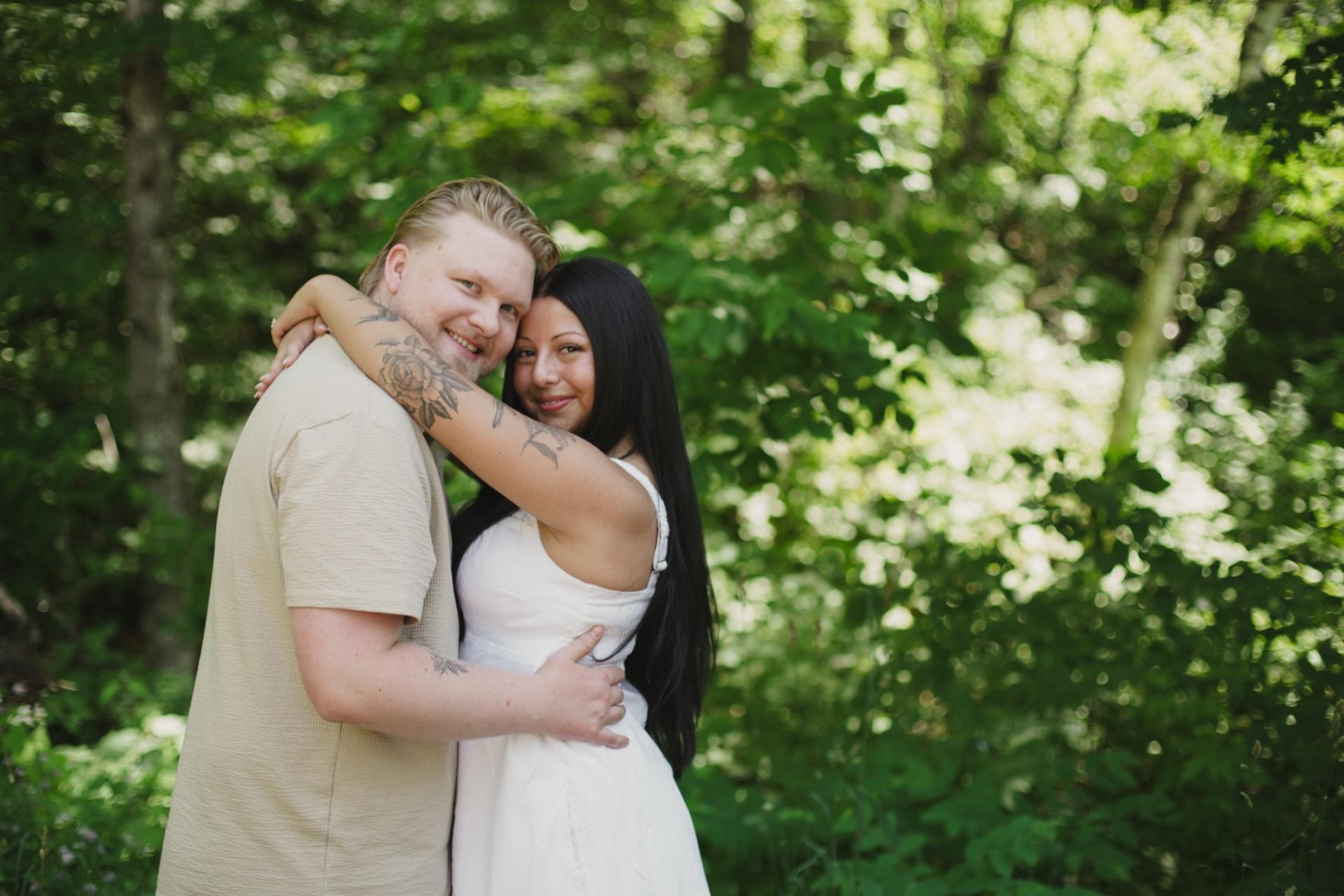 Couple embracing and smiling at the camera in bright green summer woodland