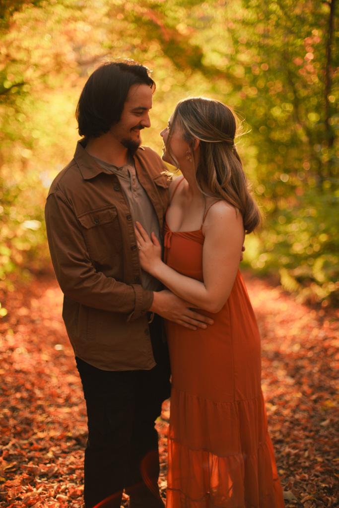Couple embracing on an autumn trail, faces close, warm light through the trees