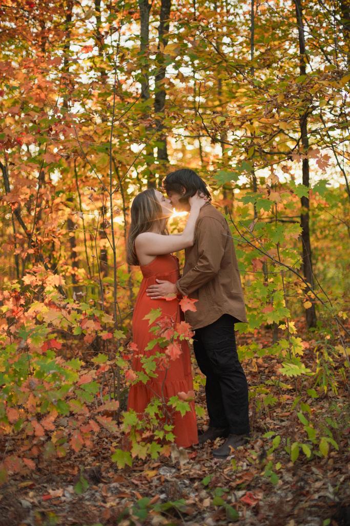 Couple kissing among orange and yellow maple leaves in autumn woods