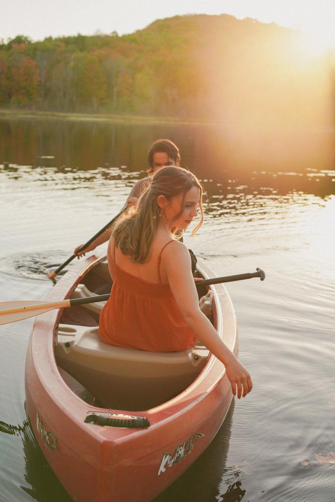 Couple paddling a red canoe across a lake at golden hour, autumn hills behind