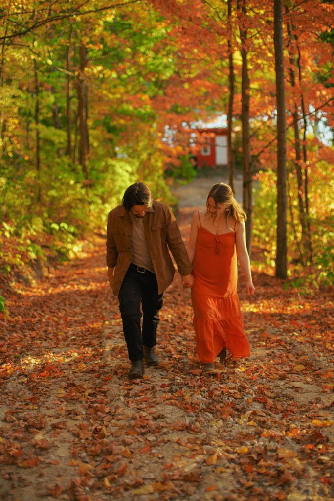 Couple laughing as they walk a leaf-covered trail through autumn woods