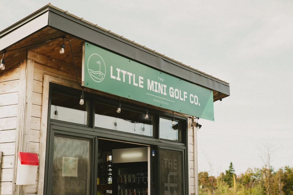 The Little Mini Golf Co sign above the shop entrance, string lights along the roof line