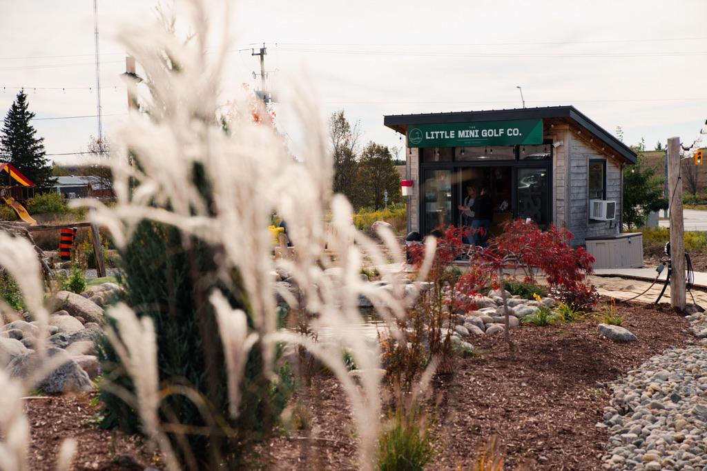 The shop seen across ornamental grasses and a red maple beside the pond