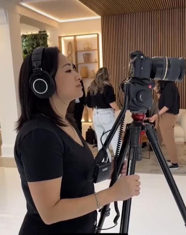 Rosa Park in headphones beside a camera on a tripod, monitoring sound on a shoot