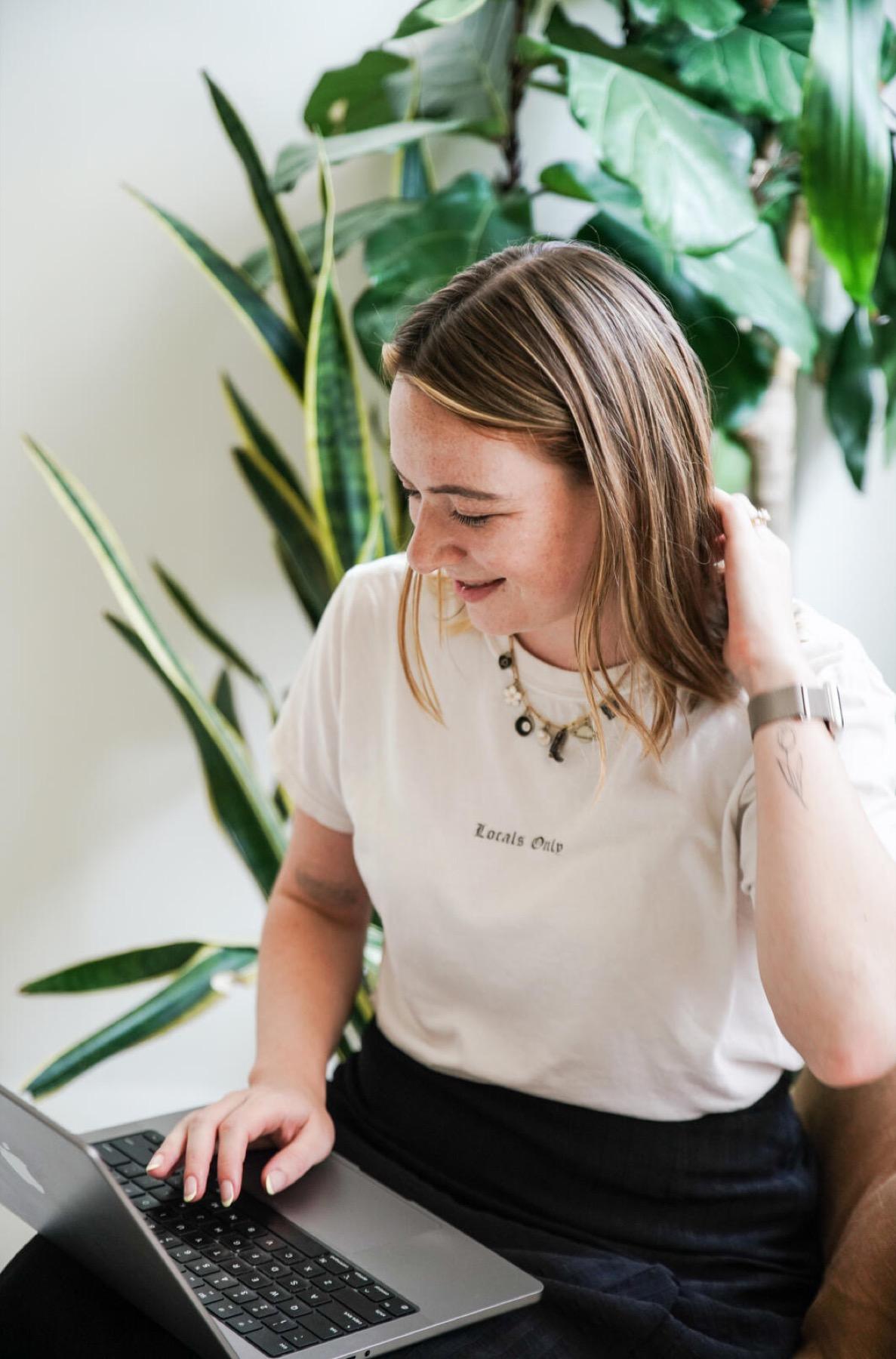 Business owner working at a laptop beside large houseplants in a bright room