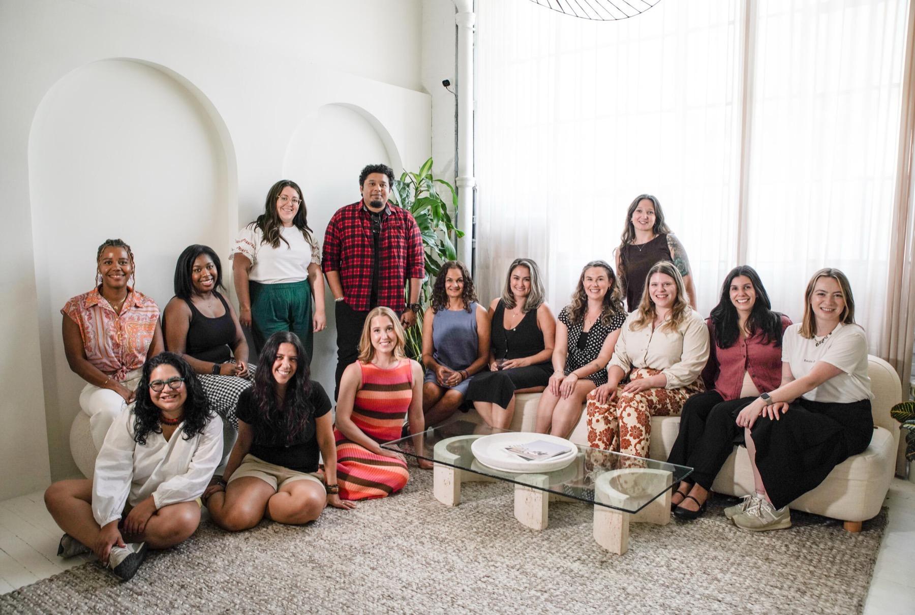 Group photograph of a fifteen-person team in a bright studio with arched alcoves
