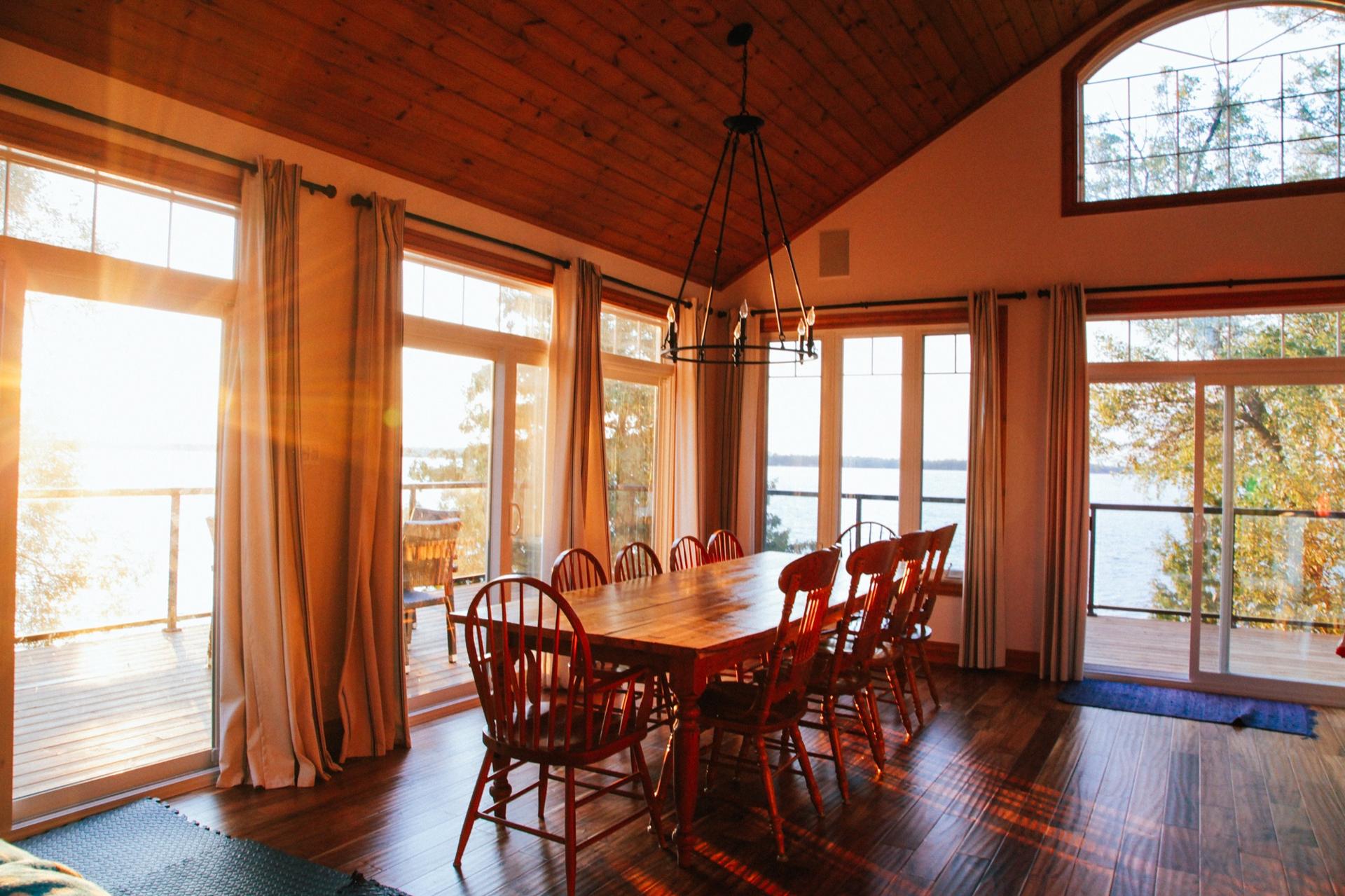 Cottage dining room with a long table, pine ceiling and low sun coming off the lake through full-height windows