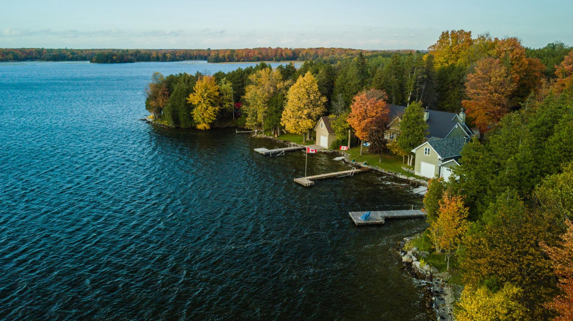 Aerial view of a waterfront cottage with a dock and boathouse on a lake, surrounded by autumn maples