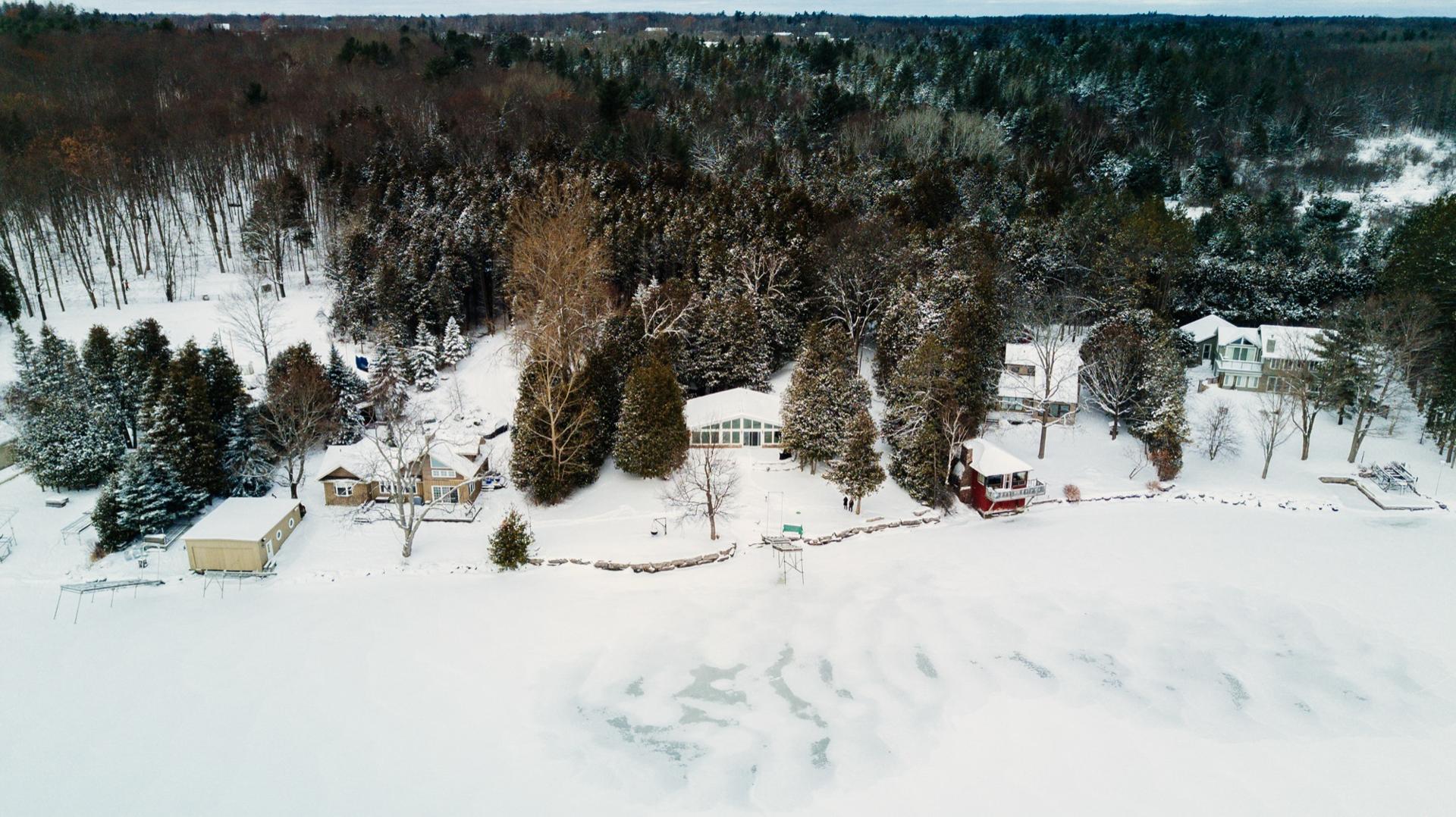 Aerial view of snow-covered waterfront cottages beside a frozen lake in winter
