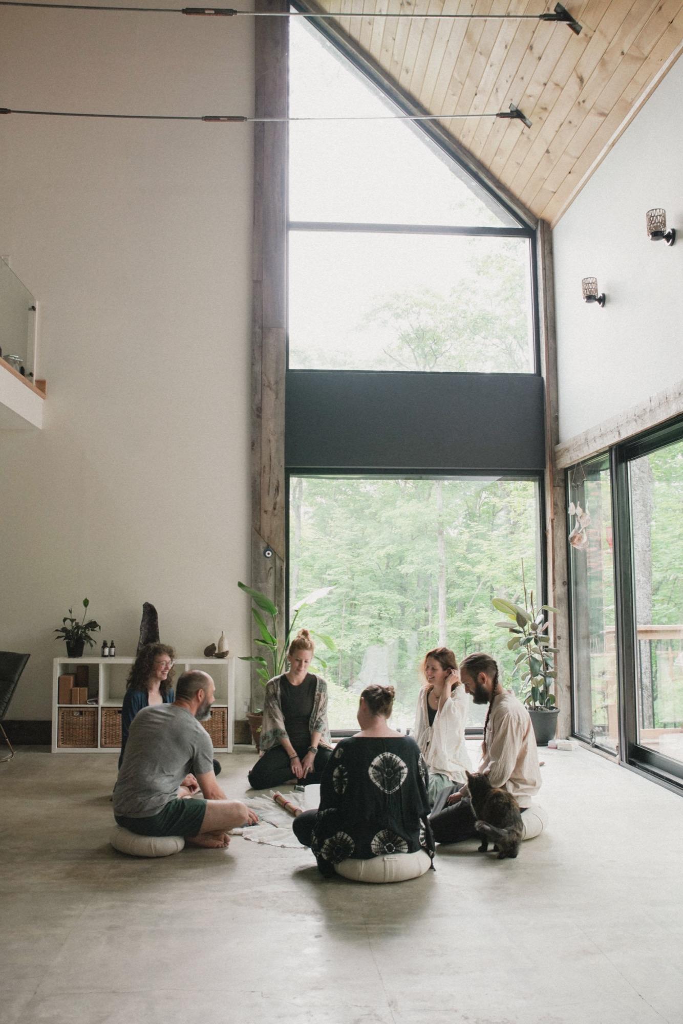 Group sitting in a circle on cushions beneath tall windows in a double-height room