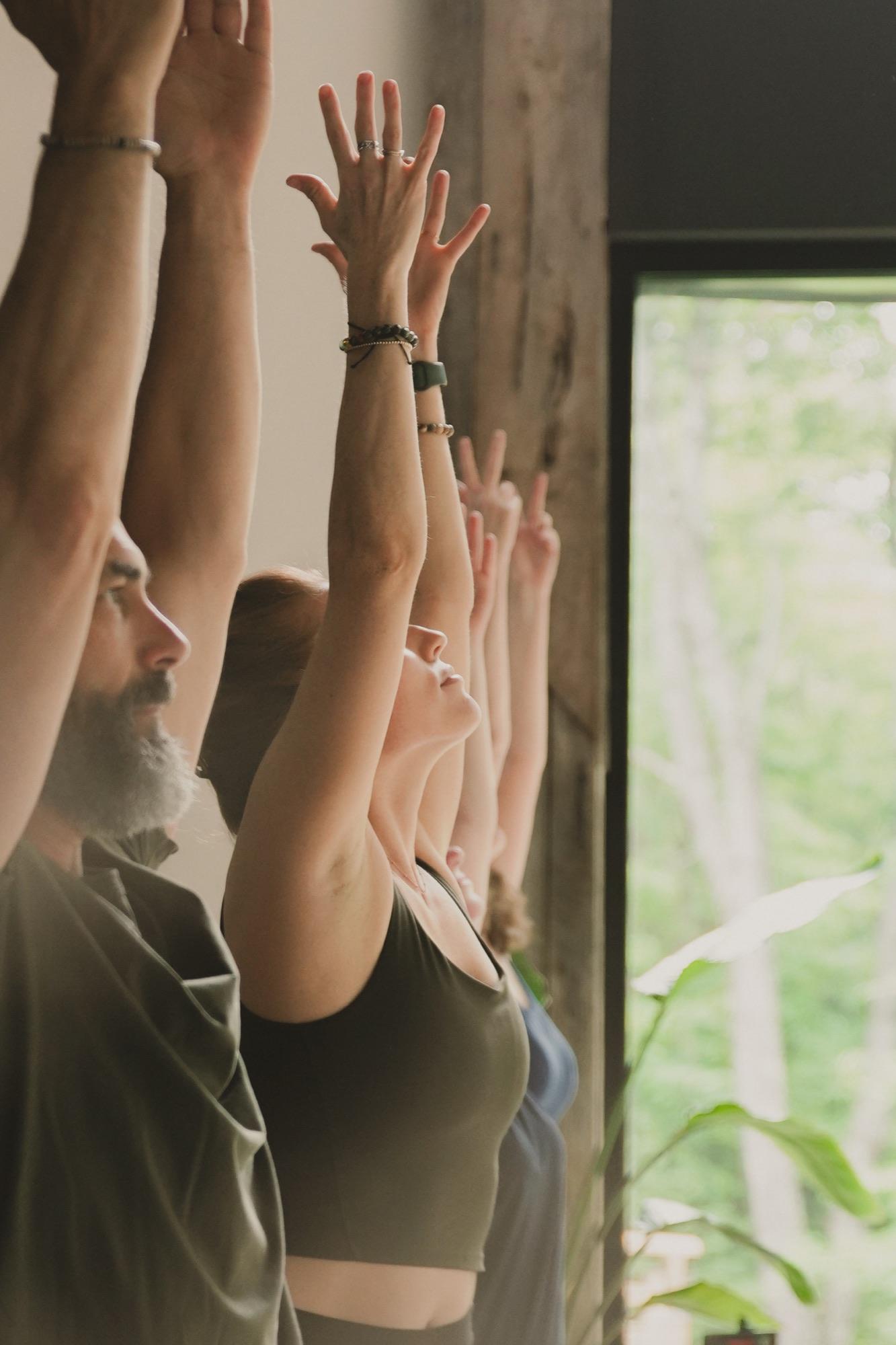 Close frame of raised hands and faces in a row during a yoga class, warm side light