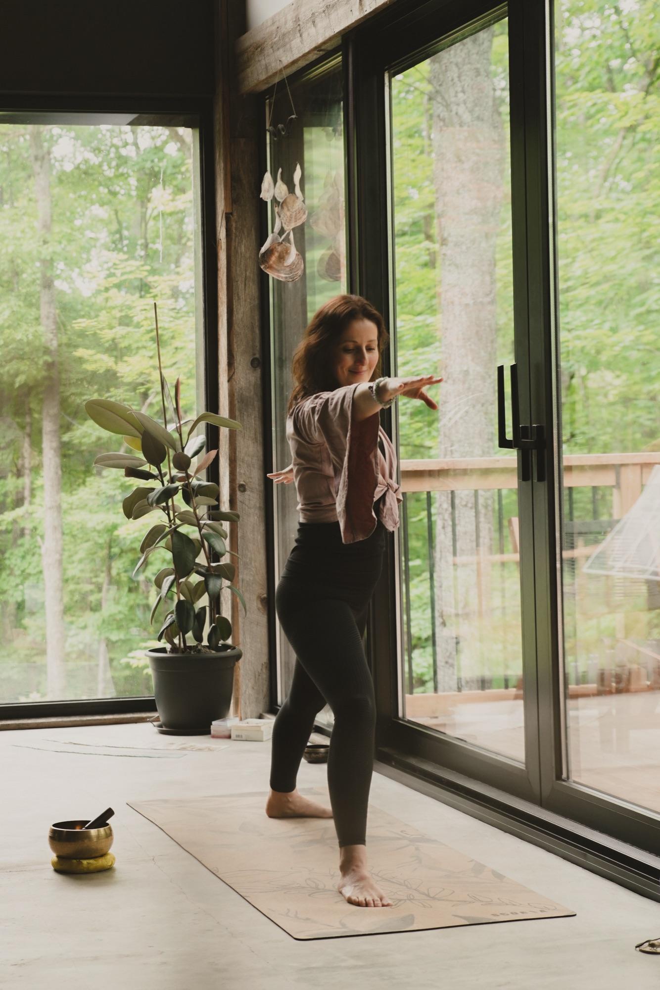Practitioner moving through a pose beside sliding doors onto a forest deck