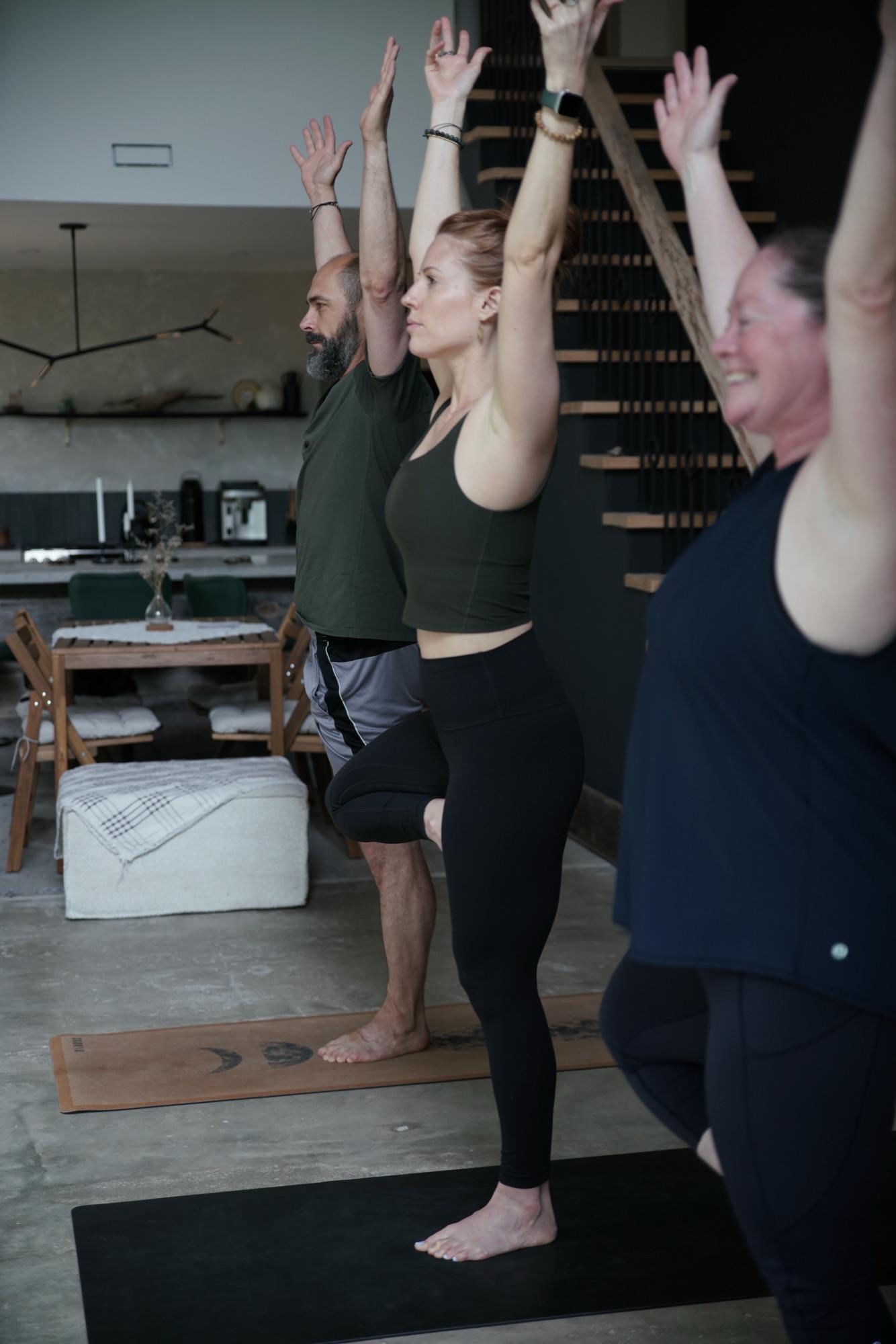 Small group balancing in tree pose in an open living space beside a dining table
